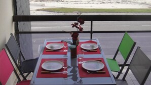 A dining table set for four with red placemats and white plates, overlooking a beach with rocks and calm water. - Apartment in quiet residence facing the beach with sea view (Quiberon)
