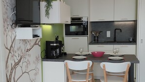 A modern kitchen with white cabinets, a black microwave, and a green accent wall. There is a dining table with two chairs and a red bowl. - Apartment in quiet residence facing the beach with sea view (Quiberon)