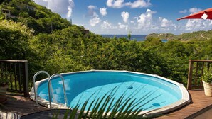 A swimming pool on a wooden deck with a view of a coastal landscape.
