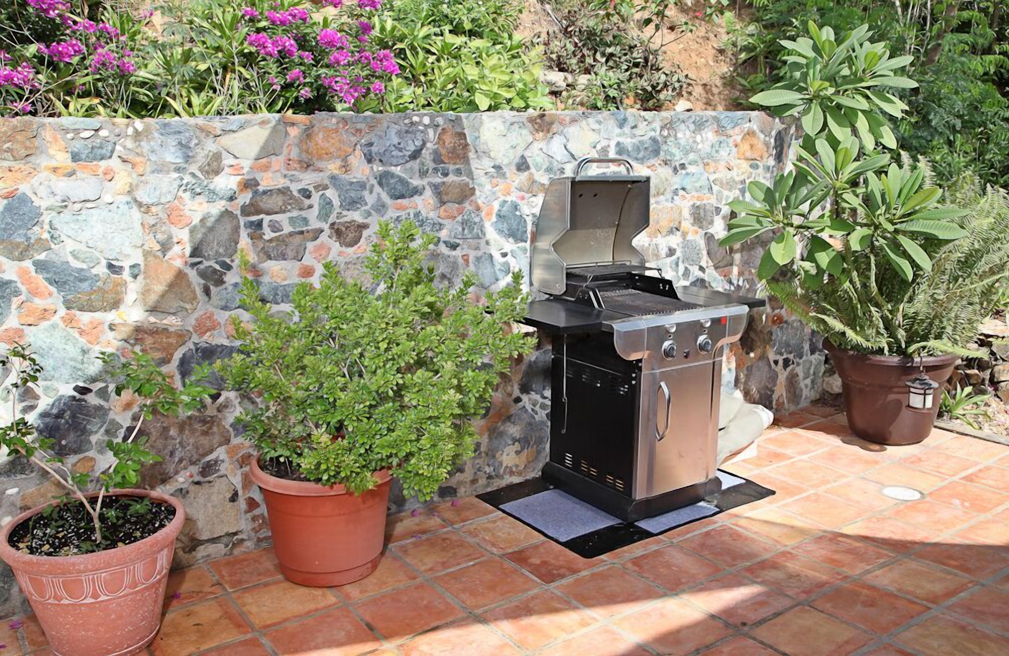 A stone wall with a barbecue grill and potted plants.