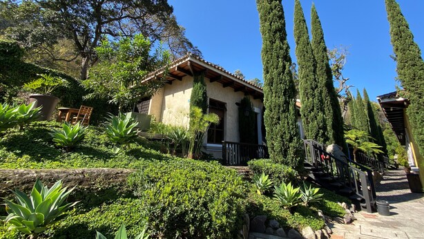 A house with a tiled roof, surrounded by lush greenery and tall cypress trees. - Cozy Studio In Quiet Condo With Heated Pool (Antigua Guatemala)