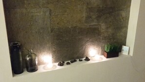 A stone wall with a shelf holding candles, a small plant, and decorative stones. - Cozy Studio In Quiet Condo With Heated Pool (Antigua Guatemala)