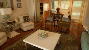 A living room with a glass coffee table, a sofa, and a dining area with chairs and a table. - Marsh-view Cottage in the Woods: surrounded by majestic oaks, birdsong & marsh! (Ridgeland)