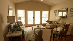 A spacious living room with a high ceiling, a dining area, and a large window providing natural light. - Marsh-view Cottage in the Woods: surrounded by majestic oaks, birdsong & marsh! (Ridgeland)