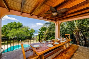 Une table de salle à manger en bois, pour quatre personnes, avec vue sur l’océan et la végétation tropicale.