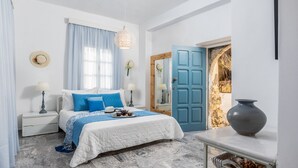 Een slaapkamer met een bed, nachtkastjes, een dressoir, een groot raam met gordijnen, een blauwe deur en een vaas op een tafel.