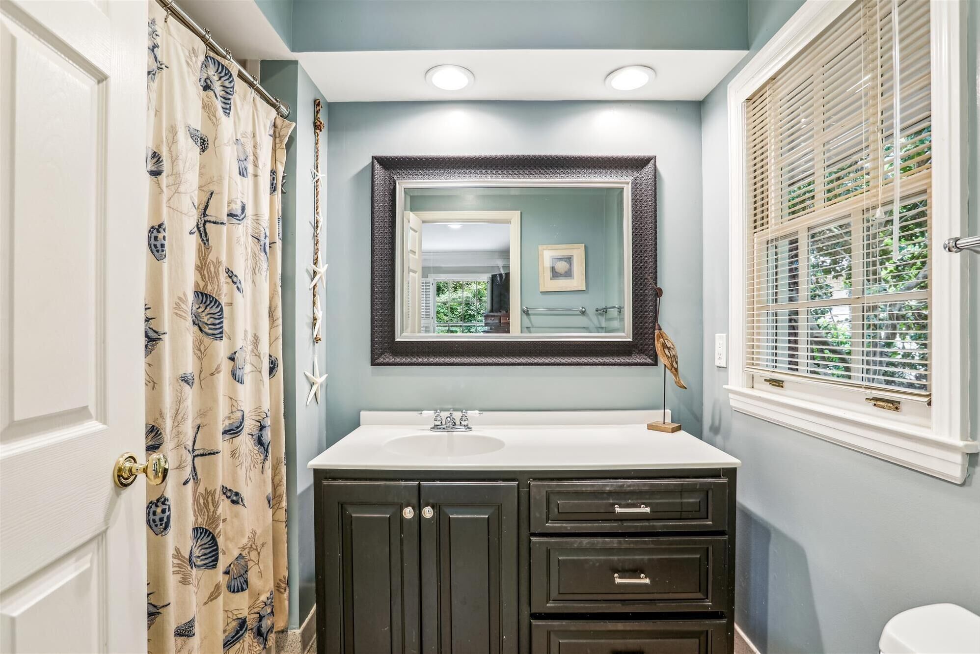 A bathroom with a vanity, a mirror, a window with blinds, and a shower curtain with a bird pattern.