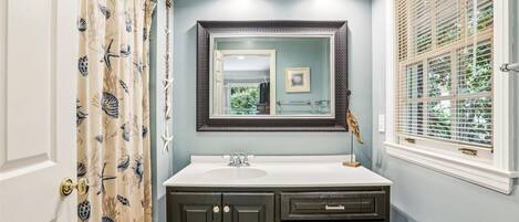 A bathroom with a vanity, a mirror, a window with blinds, and a shower curtain with a bird pattern.