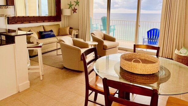 Amplia sala de estar con balcón con vistas al mar, amoblada con un sofá, sillas y una mesa de comedor.