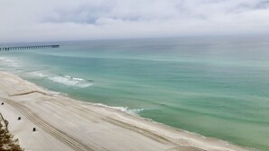 Una playa con un muelle que se adentra en el océano, orilla arenosa y cielo nublado.