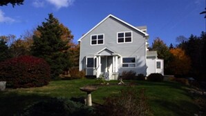A two-story house with a front porch, surrounded by a well-maintained lawn and trees.