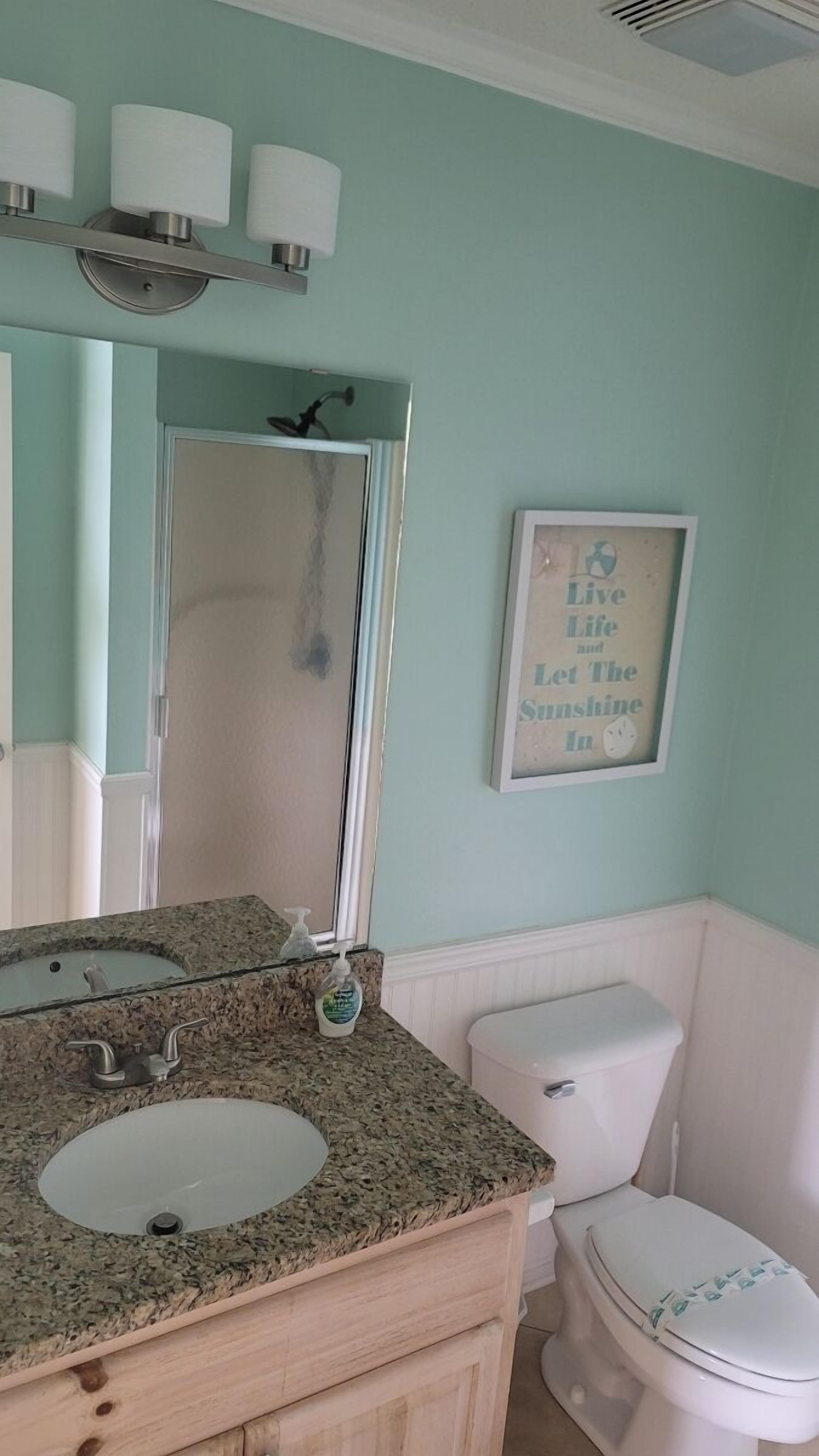 A bathroom with a granite countertop sink, a white toilet, and a framed quote on the wall.