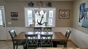 Un comedor con una mesa de madera y cuatro sillas, una lámpara de araña y adornos con forma de peces en la pared.