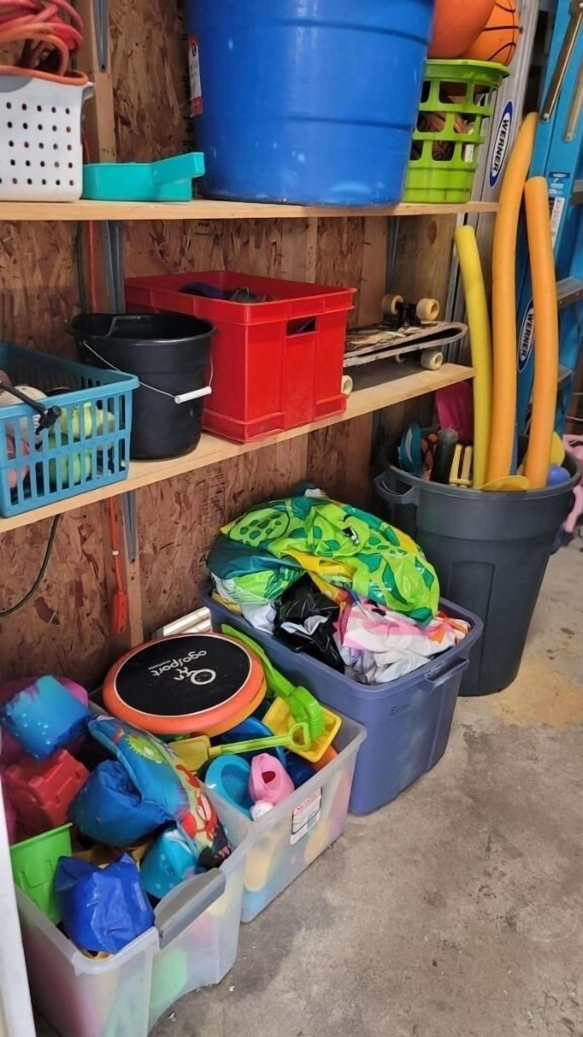 A storage area with shelves holding various items including plastic bins, a blue barrel, and sports equipment.