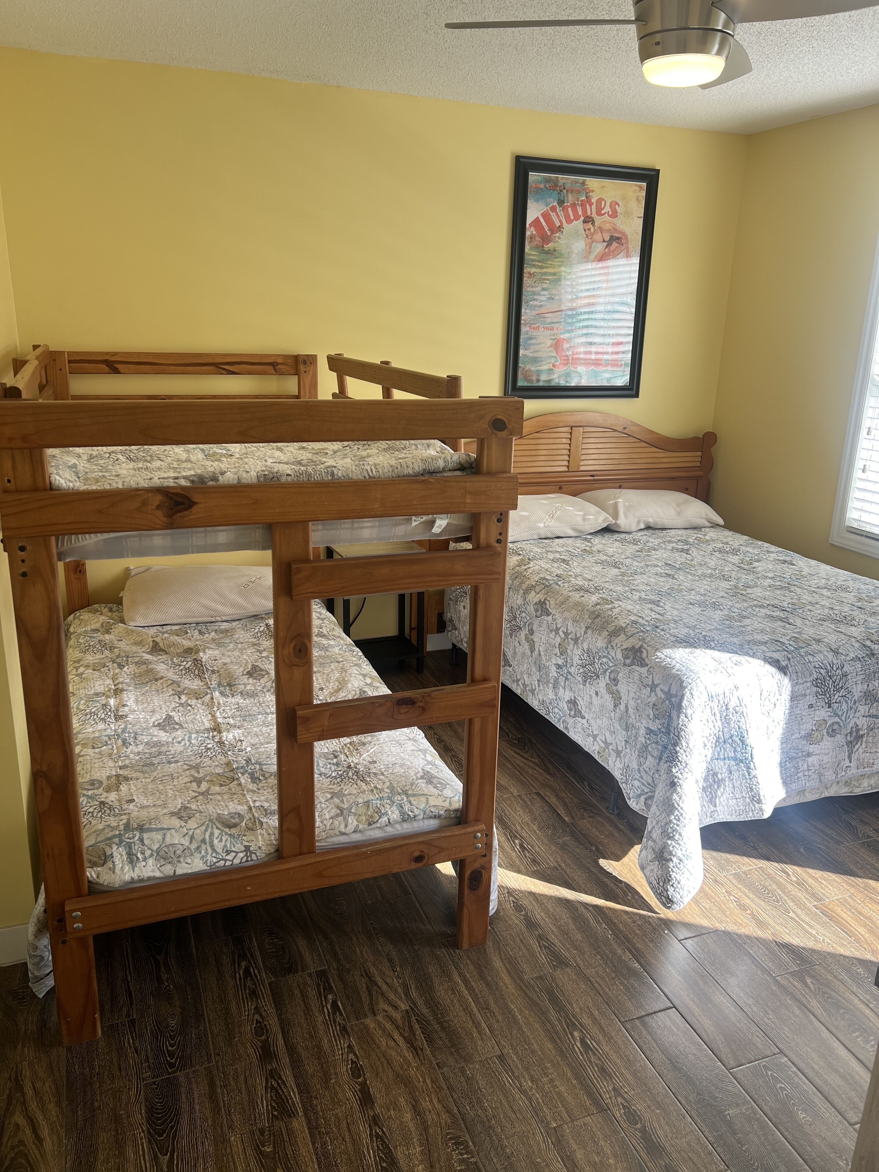 A bunk bed room with wooden frames and patterned bedding, a ceiling fan, and a framed poster on the wall.
