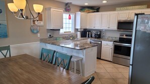 Una cocina moderna con armarios blancos, encimera de granito, refrigerador de acero inoxidable y un comedor con sillas de madera.
