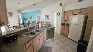 A kitchen with a dishwasher, sink, and a refrigerator. There is a dining area with chairs and a table. - 4BR Pool & Spa Home, Sleeps 8 – Near Disney, Clermont FL (Clermont)