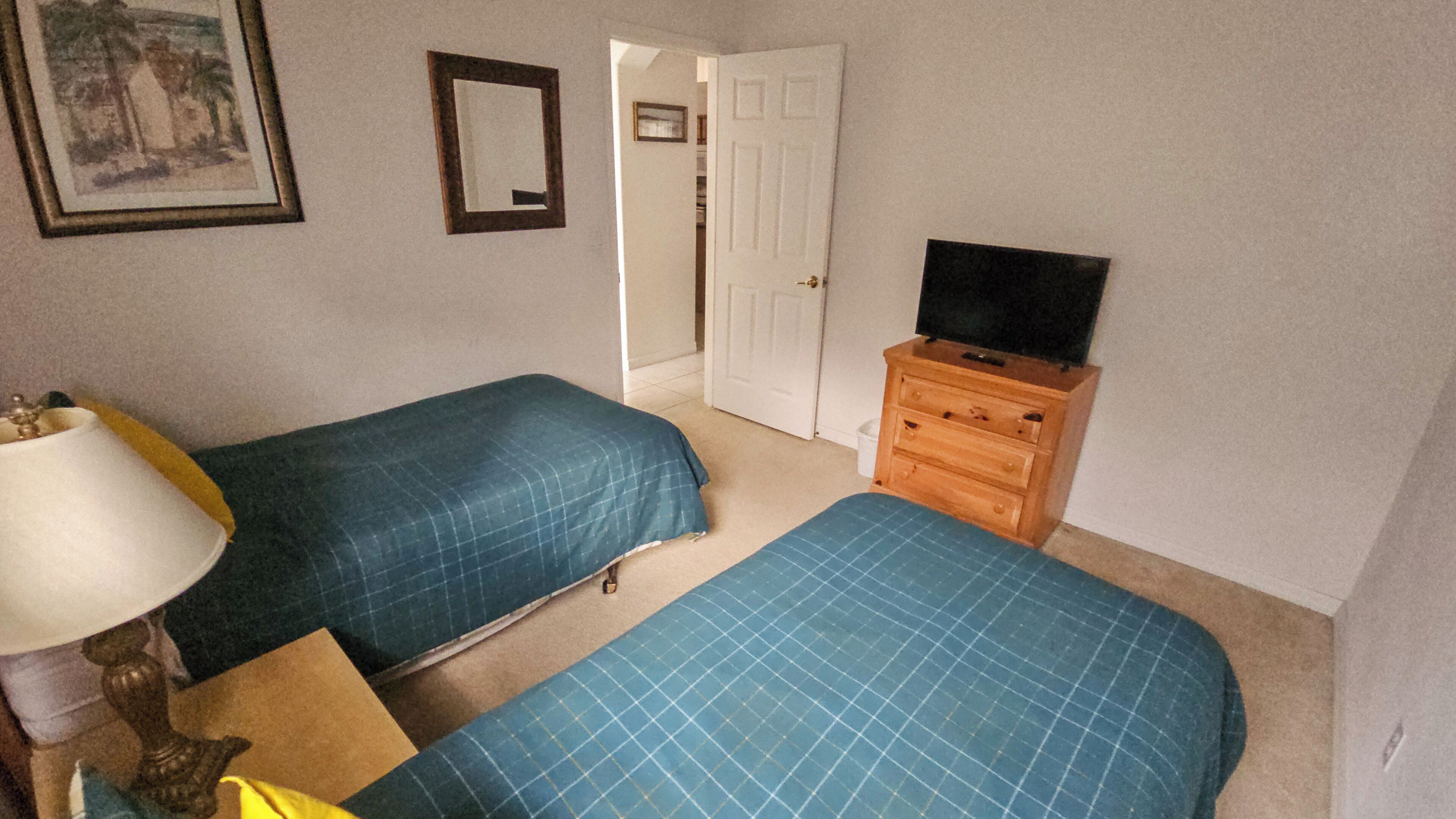 A room with two beds, a TV on a wooden dresser, a lamp, and a door leading to another room.