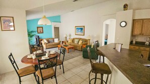 A living room with a sofa, a dining table with chairs, a kitchen area with cabinets, and a hanging light fixture. - 4BR Pool & Spa Home, Sleeps 8 – Near Disney, Clermont FL (Clermont)