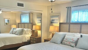 Ein Hotelzimmer mit zwei Queensize-Betten, einem Deckenventilator, einem Fenster mit Vorhängen und einem Bild an der Wand.