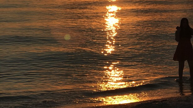 Ein Sonnenuntergang über dem Meer, mit der Silhouette einer Person am Strand.