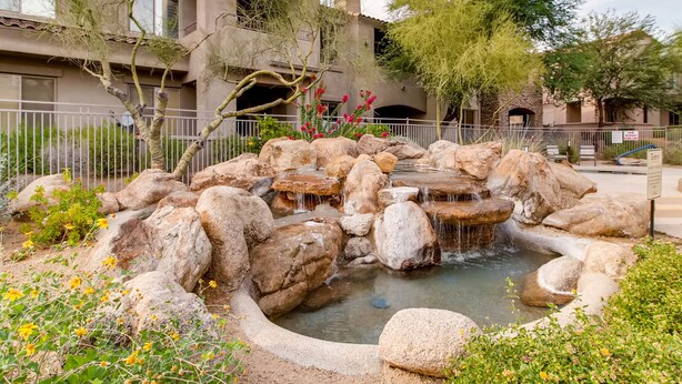 A landscaped garden with a water feature, surrounded by large rocks and flowering plants. - Grayhawk Mountain Views! Highly desirable Tesoro unit! (Scottsdale)