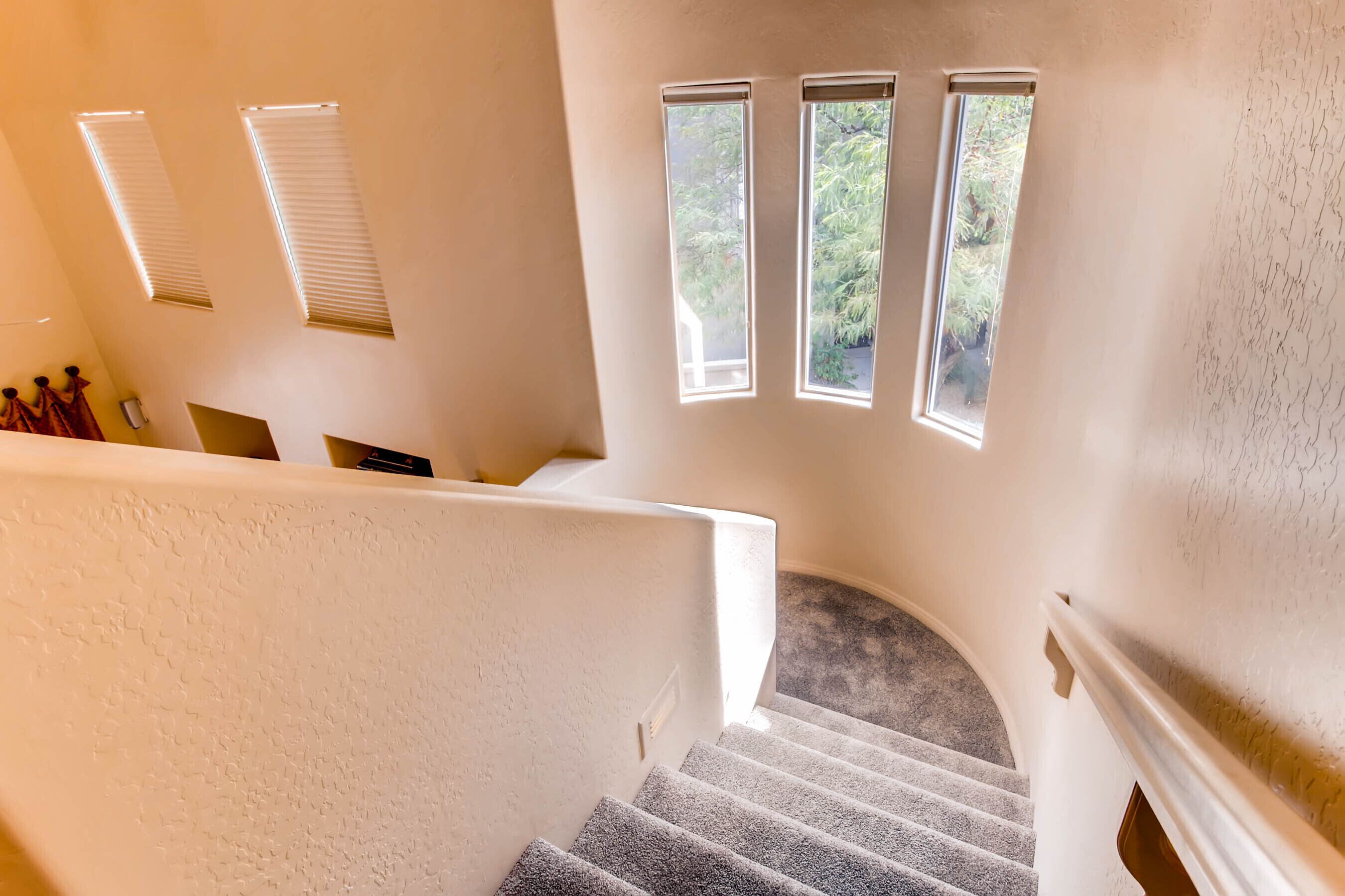 A staircase with a carpeted landing and three windows with blinds.