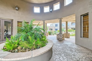A covered outdoor area with a circular planter filled with greenery, stone columns, and a stone-tiled floor.