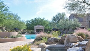 A landscaped pool area with a small waterfall, surrounded by rocks and plants. - Grayhawk Mountain Views! Highly desirable Tesoro unit! (Scottsdale)