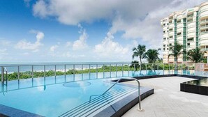 Une piscine avec vue sur l’océan et un immeuble de grande hauteur en arrière-plan.