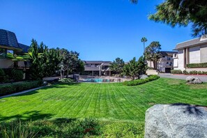 A well-maintained lawn with a swimming pool, surrounded by residential buildings and trees.