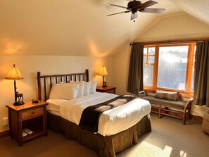 Ein gemütliches Schlafzimmer mit einem großen Bett, zwei Nachttischlampen, einem Holznachttisch, einem Sessel und einem Fenster mit Vorhängen.