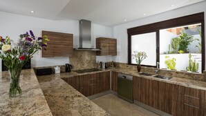 Une cuisine moderne dotée de plans de travail en granit, d’armoires en bois, d’une hotte en acier inoxydable et d’un lave-vaisselle.