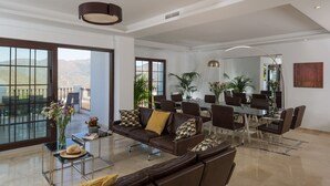 Un vaste espace de vie avec une grande porte vitrée donnant sur un balcon, un coin repas avec une table en verre et un luminaire moderne au plafond.