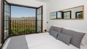 Une chambre dotée d’un grand lit, d’une table de chevet, d’un miroir et d’un balcon offrant une vue sur la montagne.
