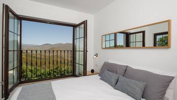 Een slaapkamer met een groot bed, een nachtkastje, een spiegel en een balkon met uitzicht op de bergen.