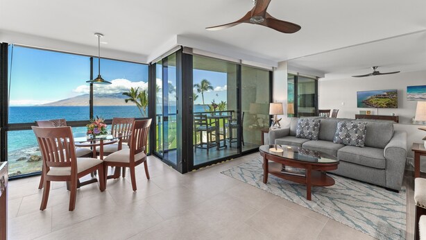 Ein modernes Wohnzimmer mit einem großen Glasfenster, das auf einen Balkon mit Meer- und Bergblick führt.