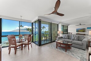Een moderne woonkamer met een grote glazen deur die uitkomt op een balkon met uitzicht op zee en een berg.