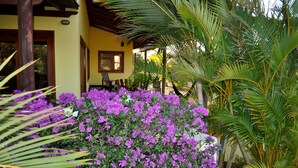 A building with a yellow exterior, surrounded by lush greenery and purple flowers. - Relaxing Beach House Just Steps from Nicaragua's Best Surf Breaks (San Diego)