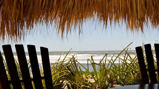 A beach view with a thatched roof structure and wooden chairs. - Relaxing Beach House Just Steps from Nicaragua's Best Surf Breaks (San Diego)