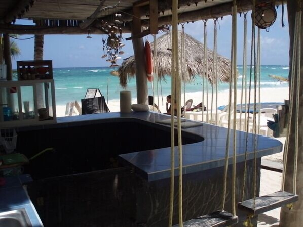 A beachside bar with a large black countertop, a thatched roof, and a view of the ocean.