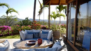 Eine Terrasse mit Sitzgelegenheiten im Freien, umgeben von üppiger Bepflanzung und Blumen, mit Blick auf eine schöne Landschaft.