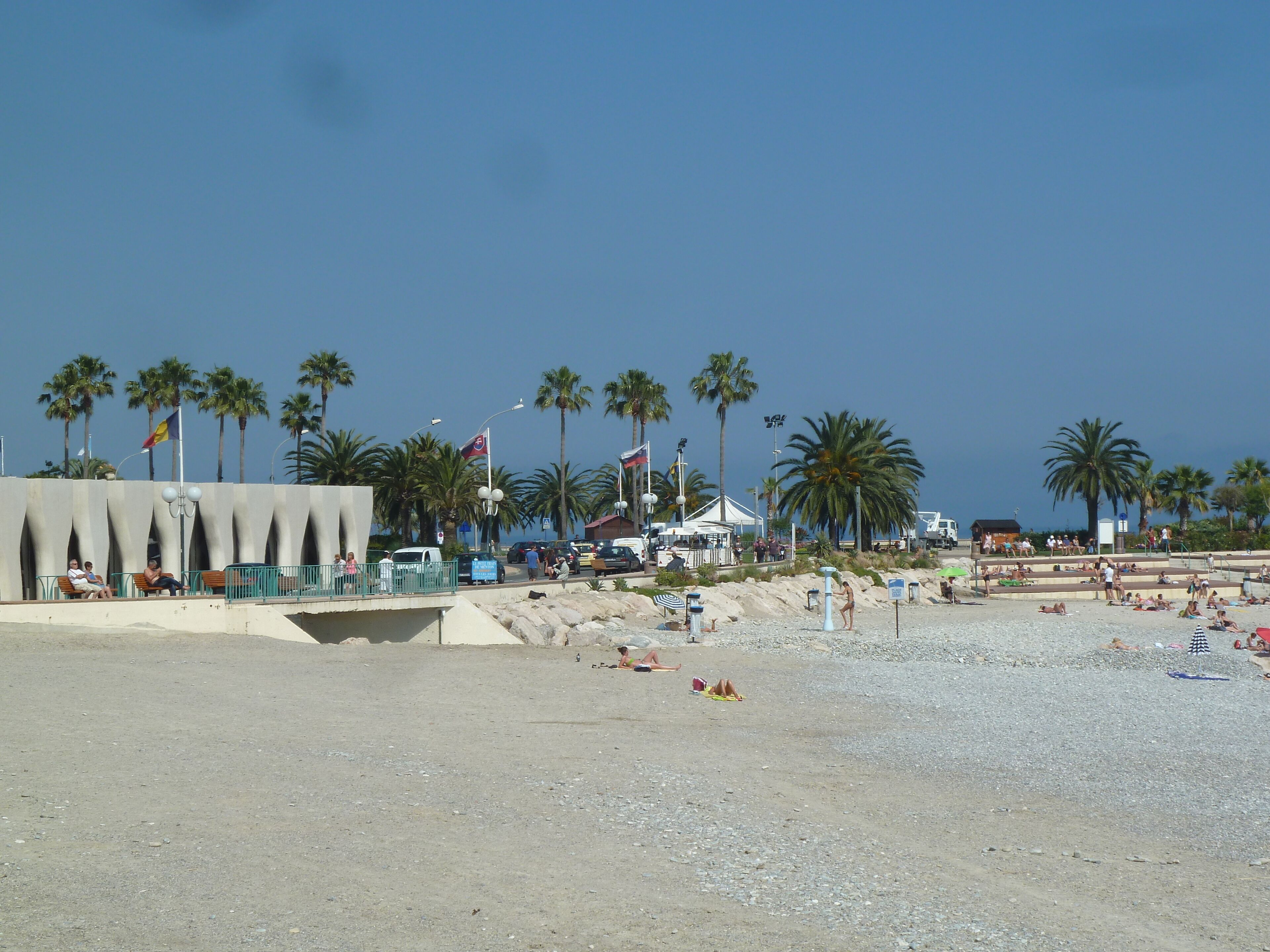 A beach with palm trees, a tent, and people sunbathing.
