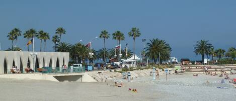 A beach with palm trees, a tent, and people sunbathing.