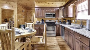 Cocina de cabaña de madera con una mesa y sillas dispuestas, un microondas, estufa y un lavamanos.