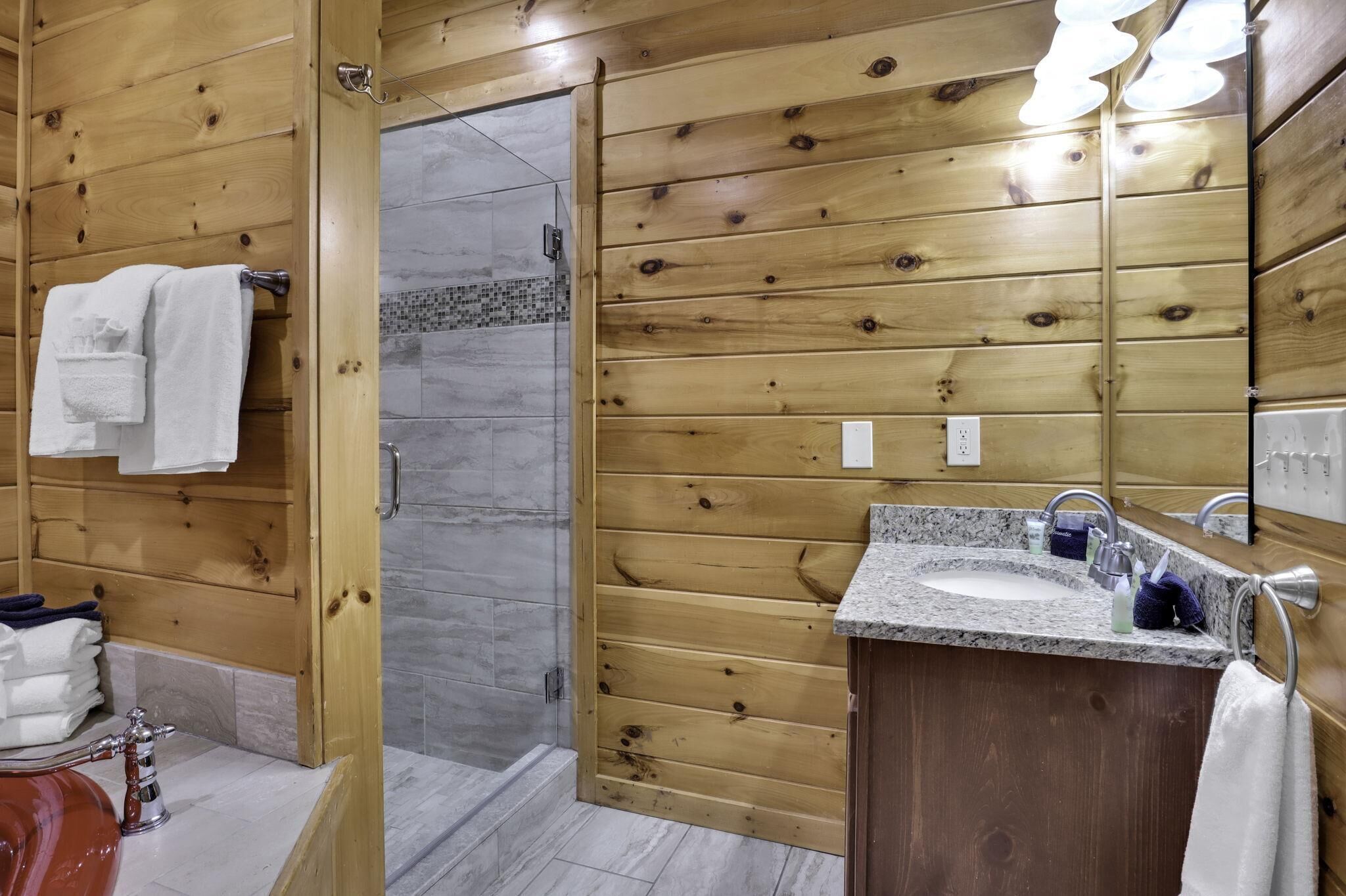 A wooden-paneled bathroom with a granite sink, a mirror, and a shower area.