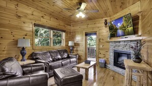 Un interior de cabaña acogedor con un sofá de cuero, una chimenea, un televisor y paredes de madera.
