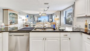 Une cuisine moderne avec des meubles blancs, un lave-vaisselle en acier inoxydable et un îlot central doté d’un évier.