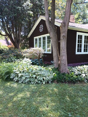 Una casa con chimenea, una ventana con diseño decorativo y un árbol en el jardín delantero.