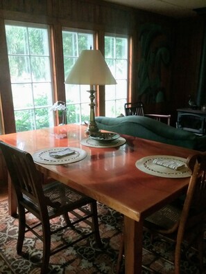 Una mesa de comedor con individuales, una lámpara y sillas en una habitación con ventanas amplias y una alfombra estampada.